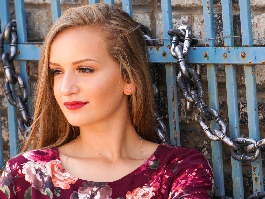 Красивая молодая девушка сидит у забора с железными цепями