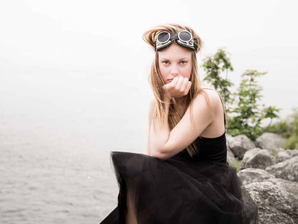 Девушка блондинка с очками на голове сидит на камне