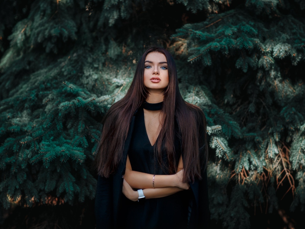 Голубоглазая девушка брюнетка у большой зеленой ели 