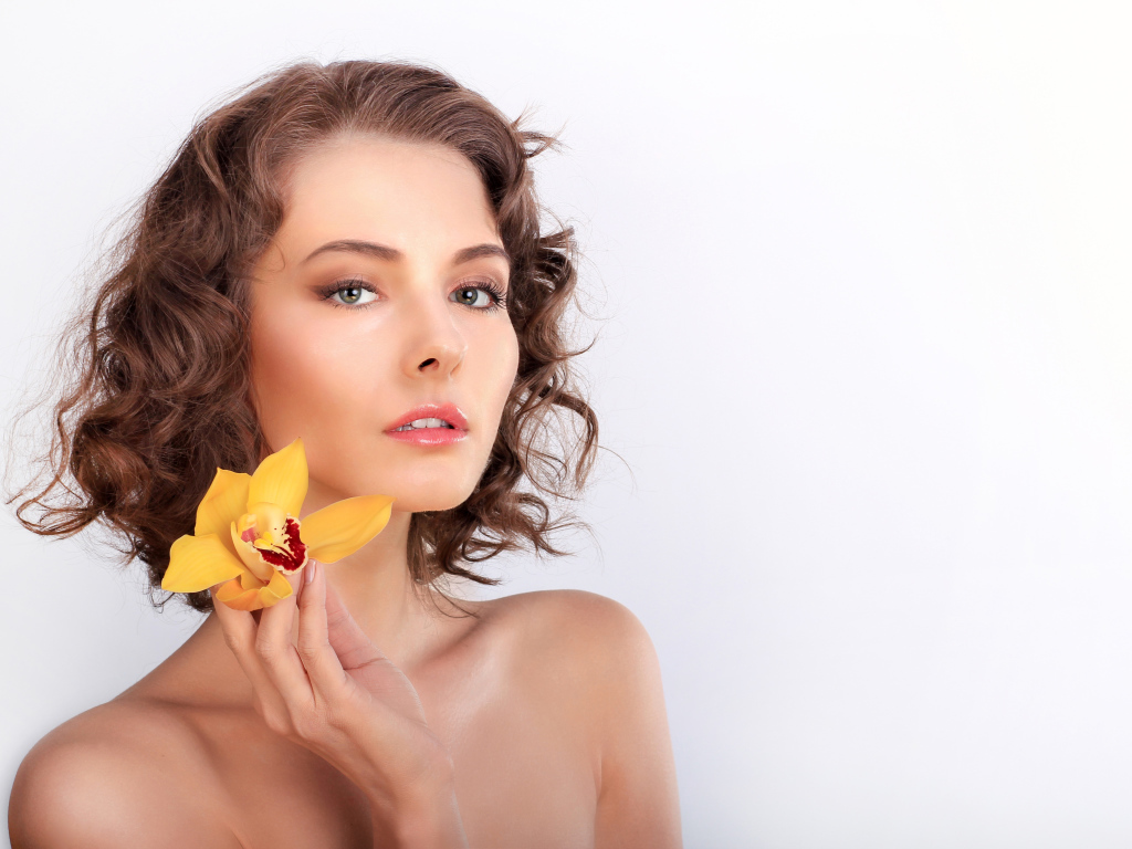 Нежная девушка шатенка с желтым цветком орхидеи в руке