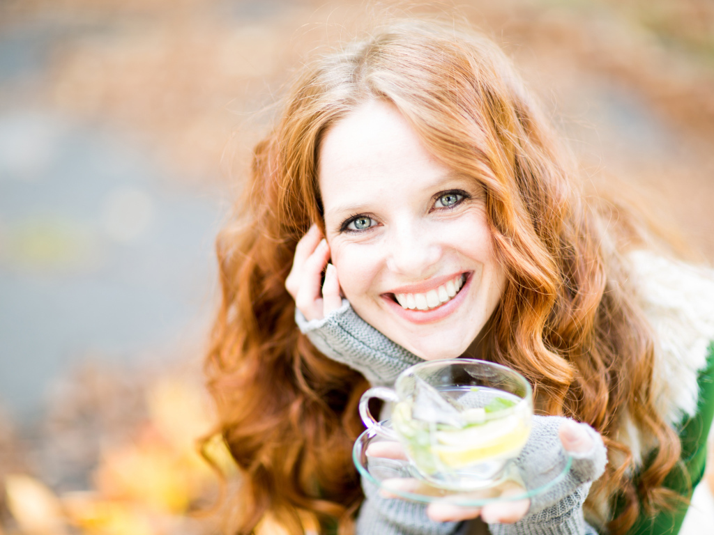 Улыбающаяся рыжеволосая девушка с чашкой чая в руке