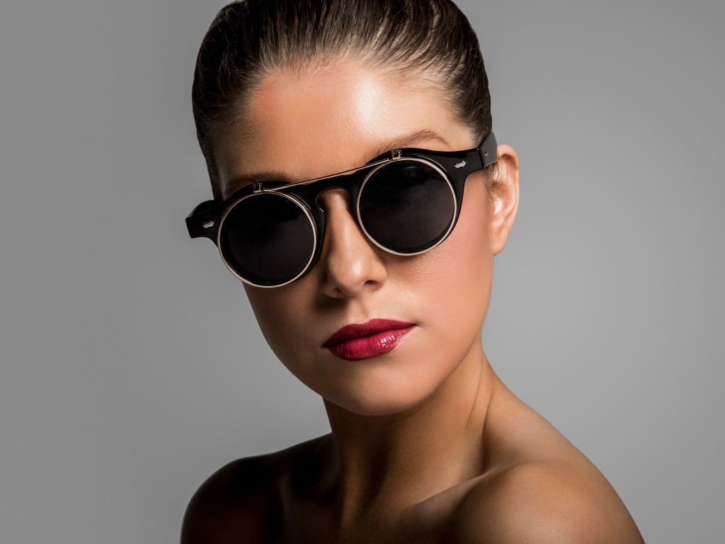 Лицо девушки в черных очках на сером фоне
