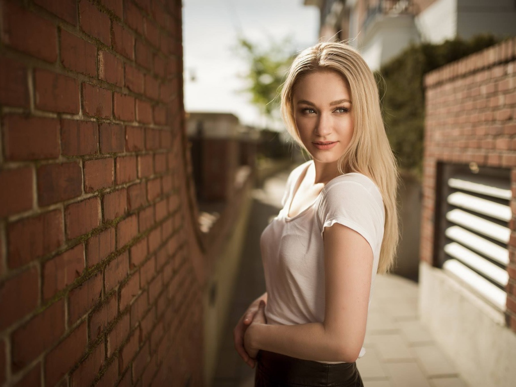 Молодая девушка блондинка у кирпичной стены 