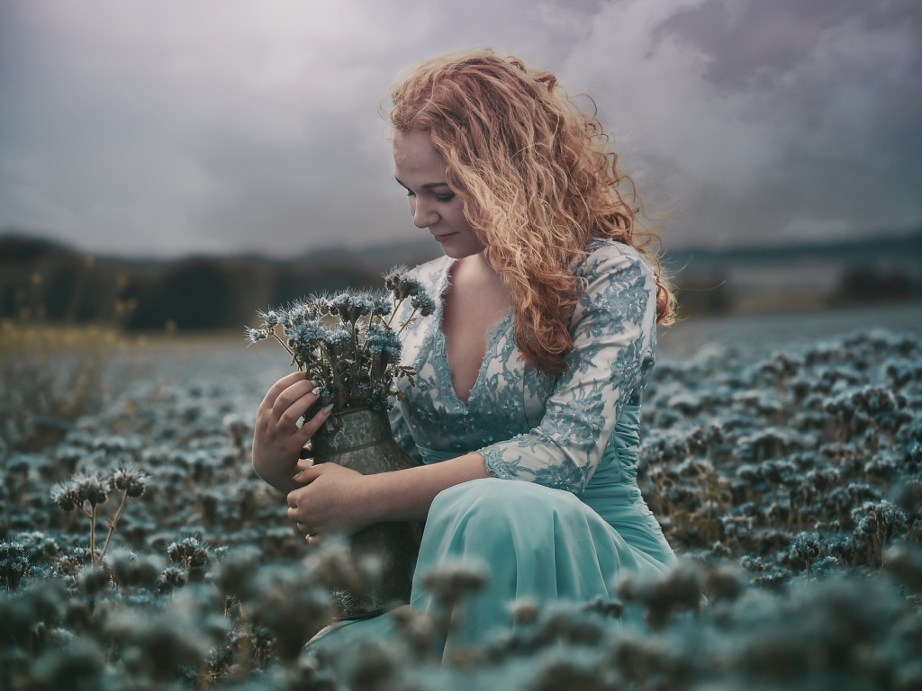 Молодая девушка собирает в кувшин голубые полевые цветы