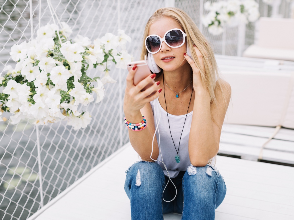 Молодая девушка в солнечных очках сидит с телефоном у белых цветов