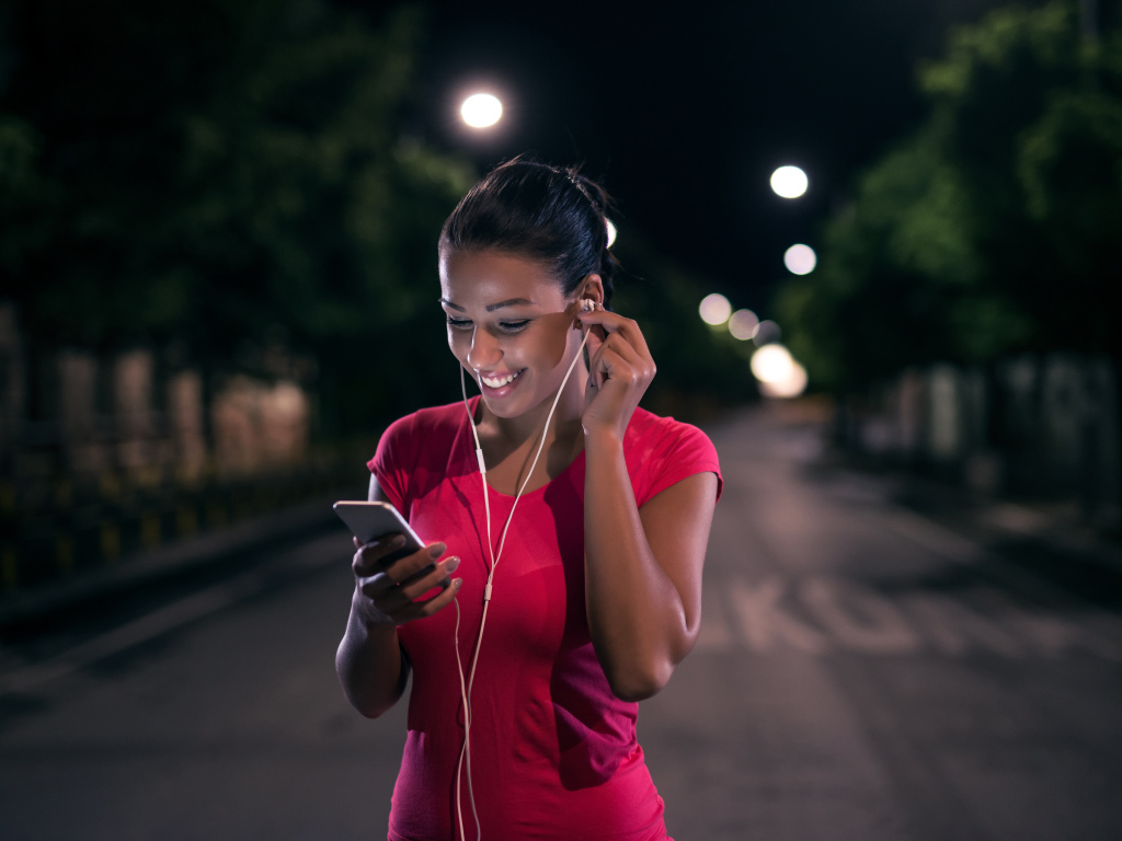 Молодая улыбающаяся девушка в наушниках с телефоном в руках