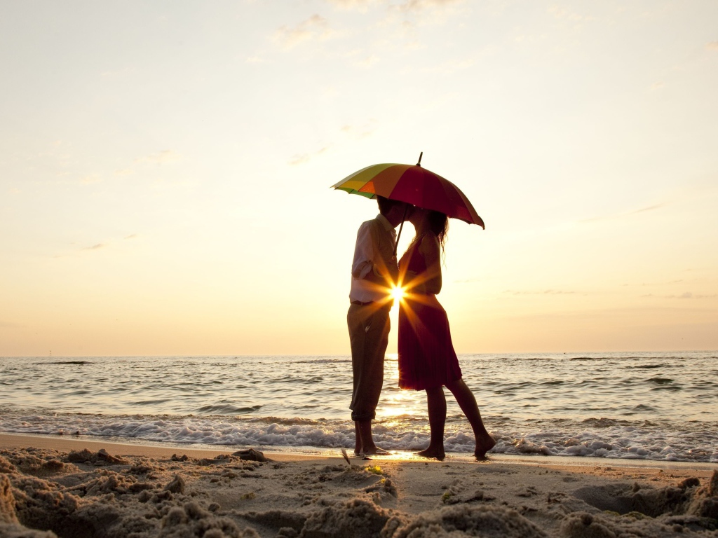 Влюбленная пара на пляже стоит под зонтом на закате