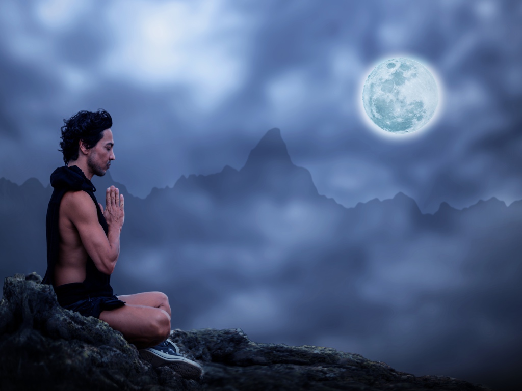 Мужчина медитирует на камне ночью в полнолуние
