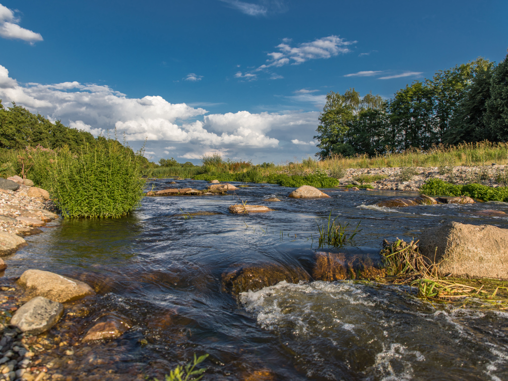 Быстрая речная вода стекает по камням под красивым голубым небом