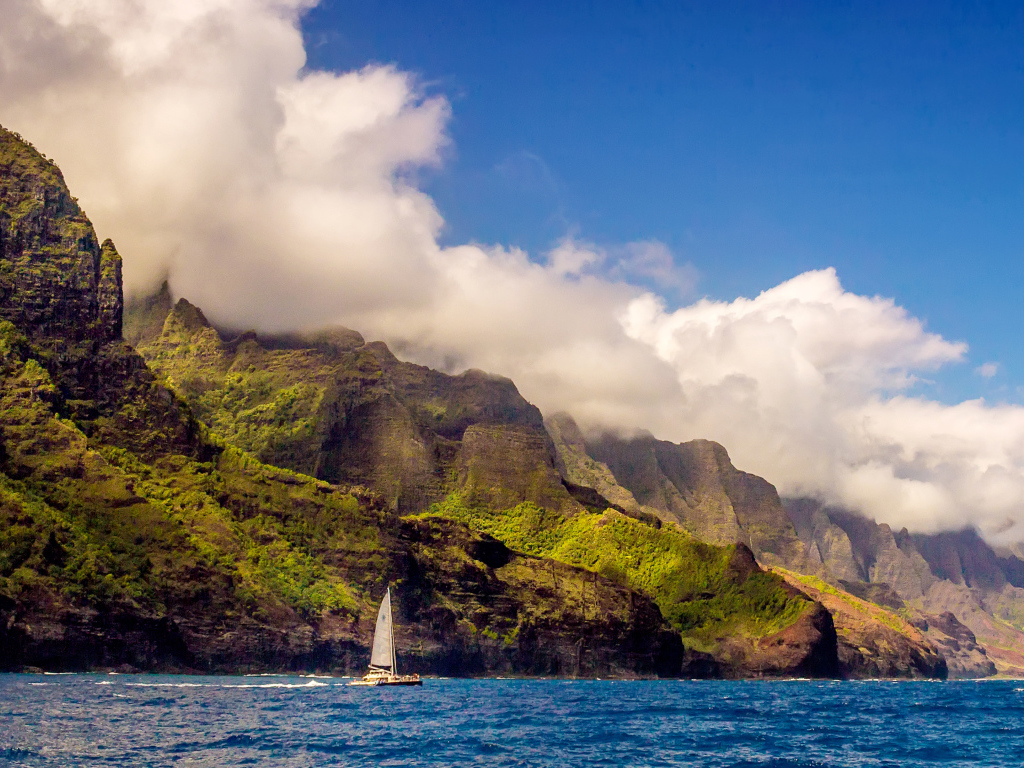 Парусная лодка плывет по голубой воде на фоне покрытых зеленью гор