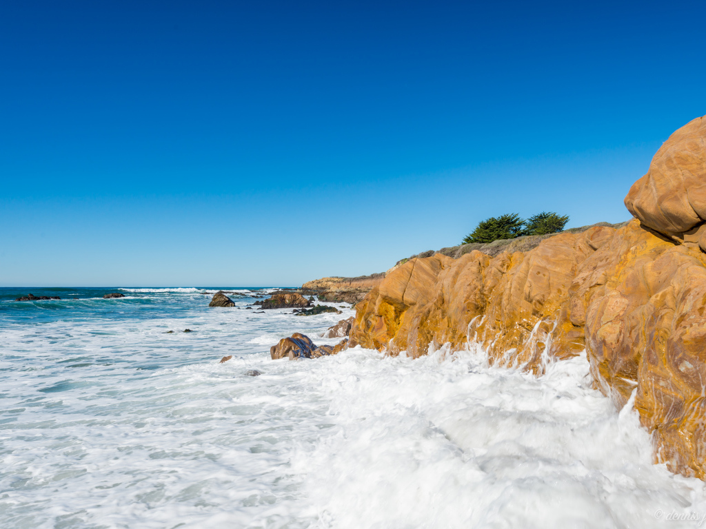 Белые волны бьются о скалы на берегу океана под голубым небом