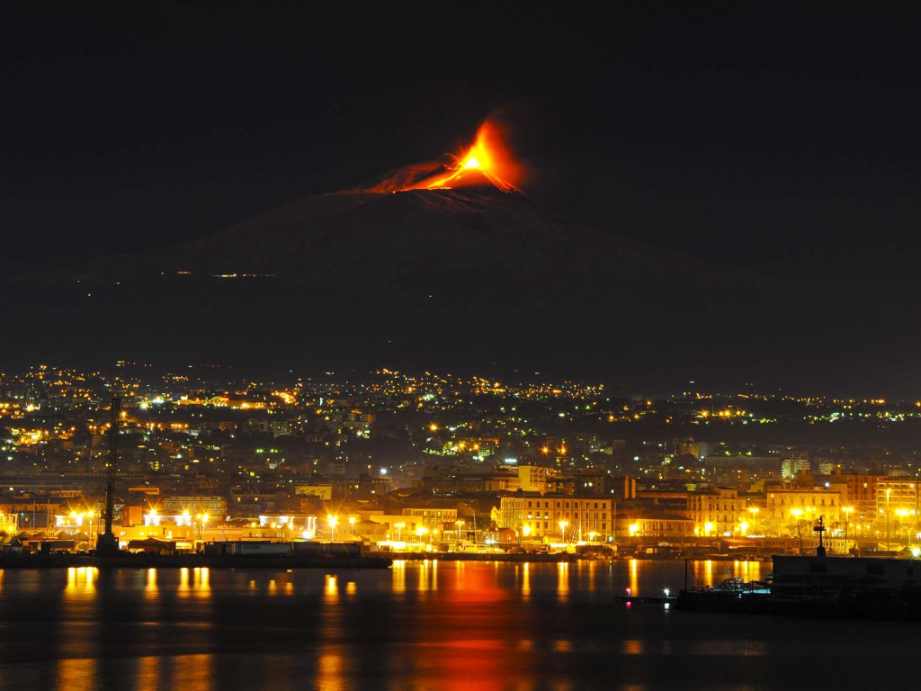 Awakening of the volcano Etna in the background of the night city