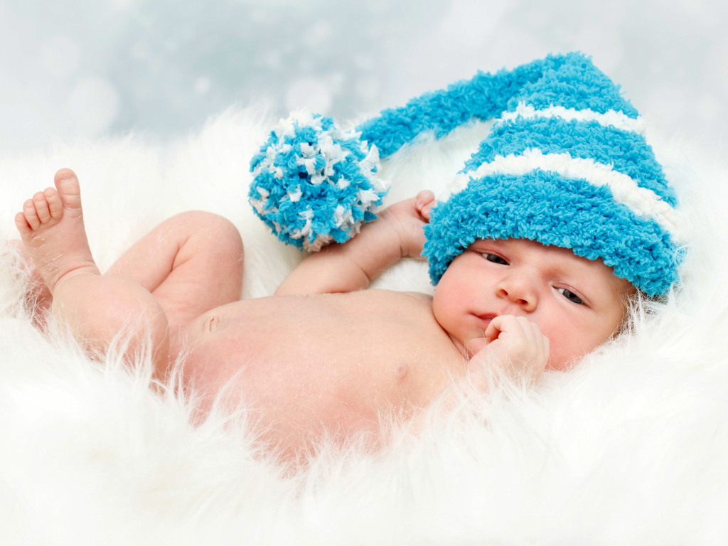 Грудной ребенок в голубой шапке с бубоном на голове