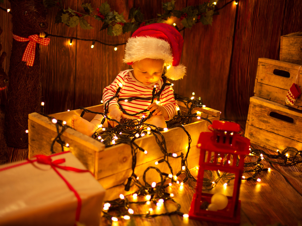 Маленький мальчик сидит в коробке с новогодней гирляндой