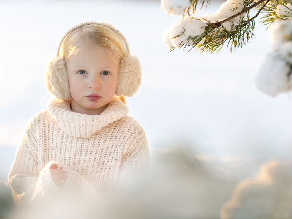 Маленькая девочка в белом свитере у покрытой снегом ели