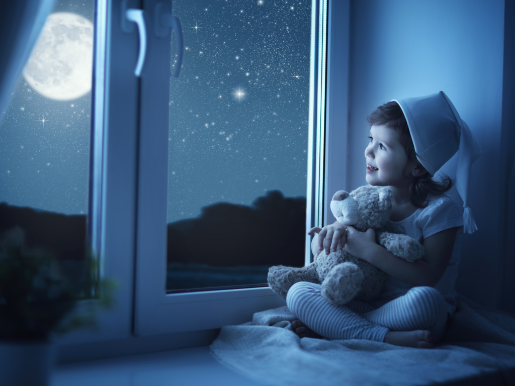 Маленькая девочка сидит на подоконнике с игрушкой ночью