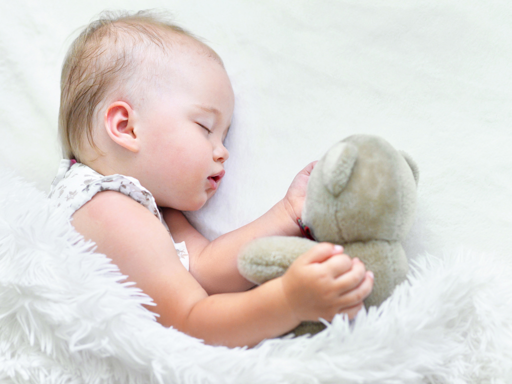 Маленькая девочка спит с мягкой игрушкой под белым одеялом