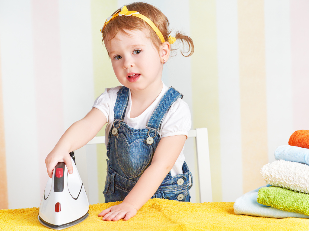 Маленькая девочка с утюгом гладит полотенце