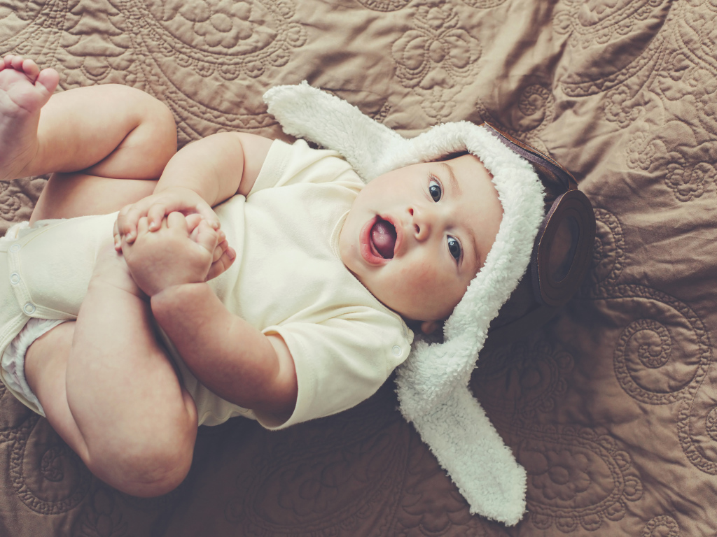 Маленький грудной ребенок лежит в шапке летчика