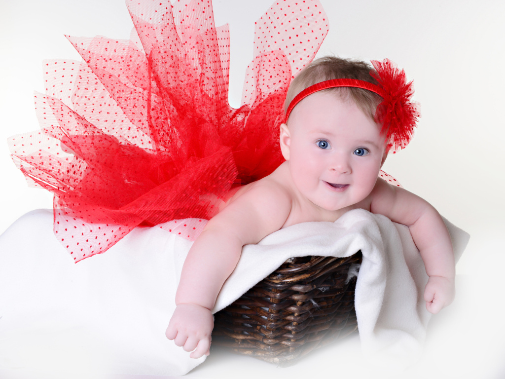 Маленькая голубоглазая девочка в красном красивом платье лежит в корзине