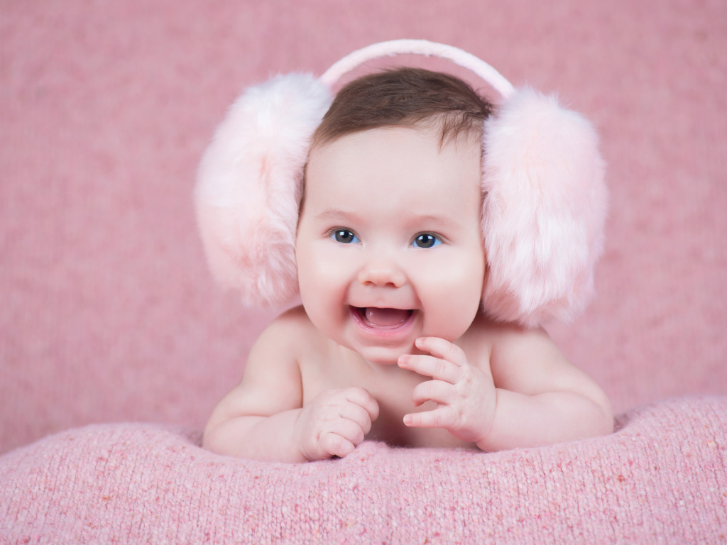 Милый улыбающийся младенец в больших розовых наушниках