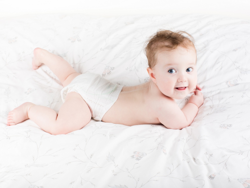 Забавный голубоглазый малыш лежит на белом покрывале