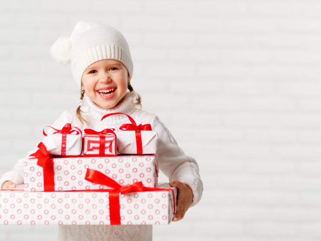 Смеющаяся девочка в белой шапке с новогодними подарками