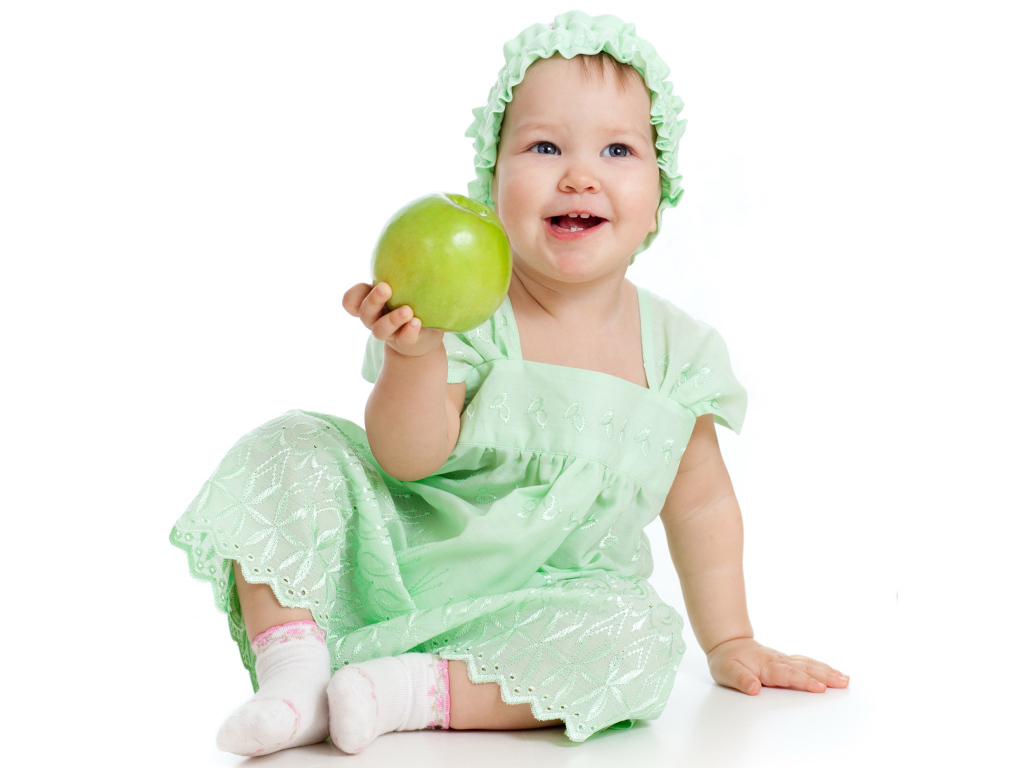 Маленькая голубоглазая девочка с зеленым яблоком в руках