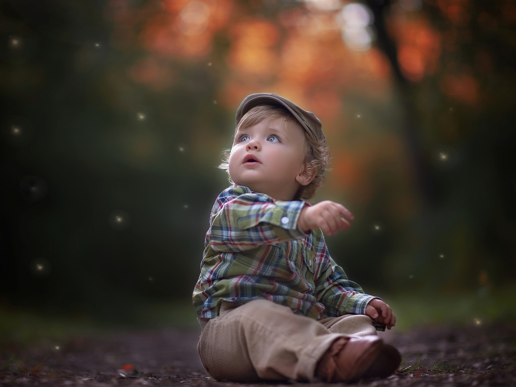 Маленький милый мальчик сидит в кепке на дороге