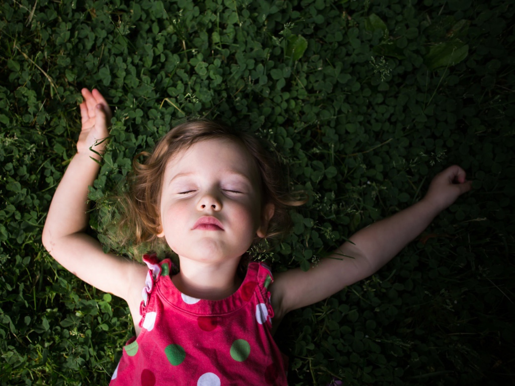 Маленькая девочка спит на зеленой траве 
