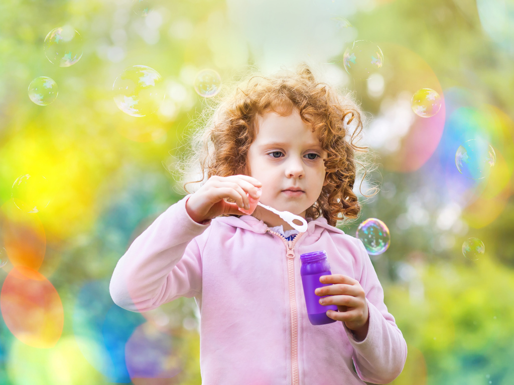 Маленькая рыжеволосая кудрявая девочка с мыльными пузырями