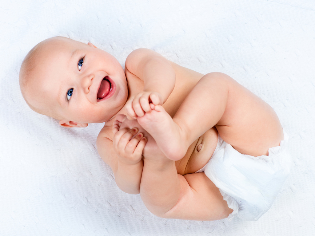 Маленький улыбающийся грудной ребенок держит руками ноги