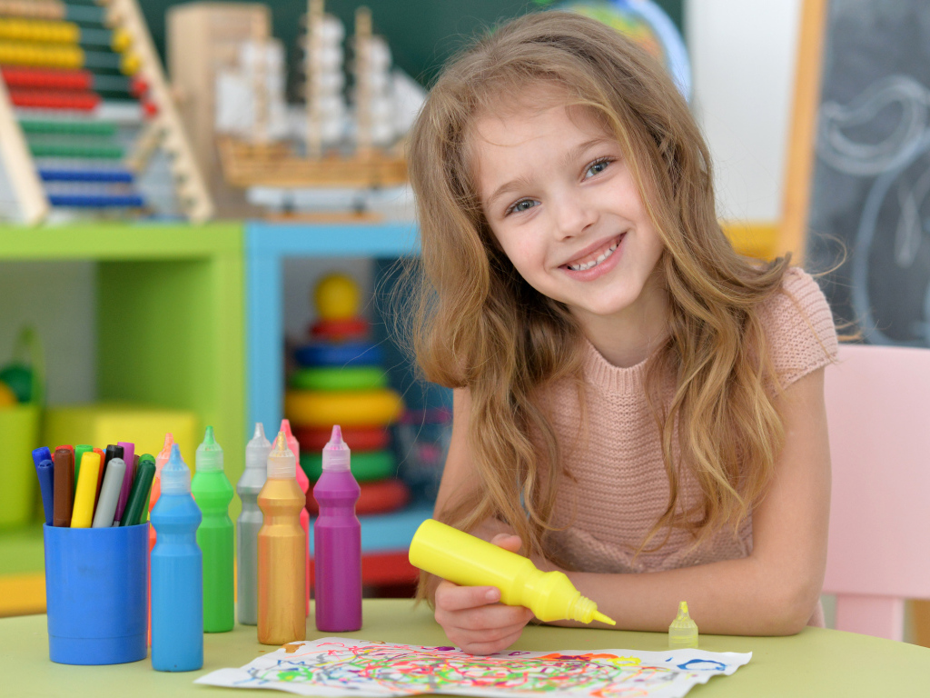 Маленькая улыбающаяся девочка рисует карандашами