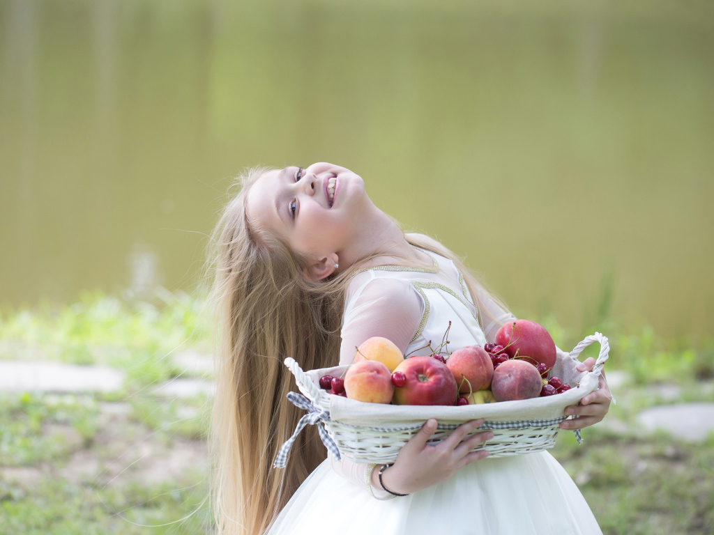 Маленькая улыбающаяся девочка в белом платье с корзиной фруктов