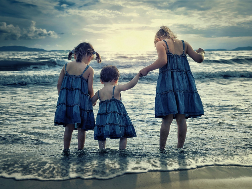 Три маленькие девочки стоят в воде на берегу моря