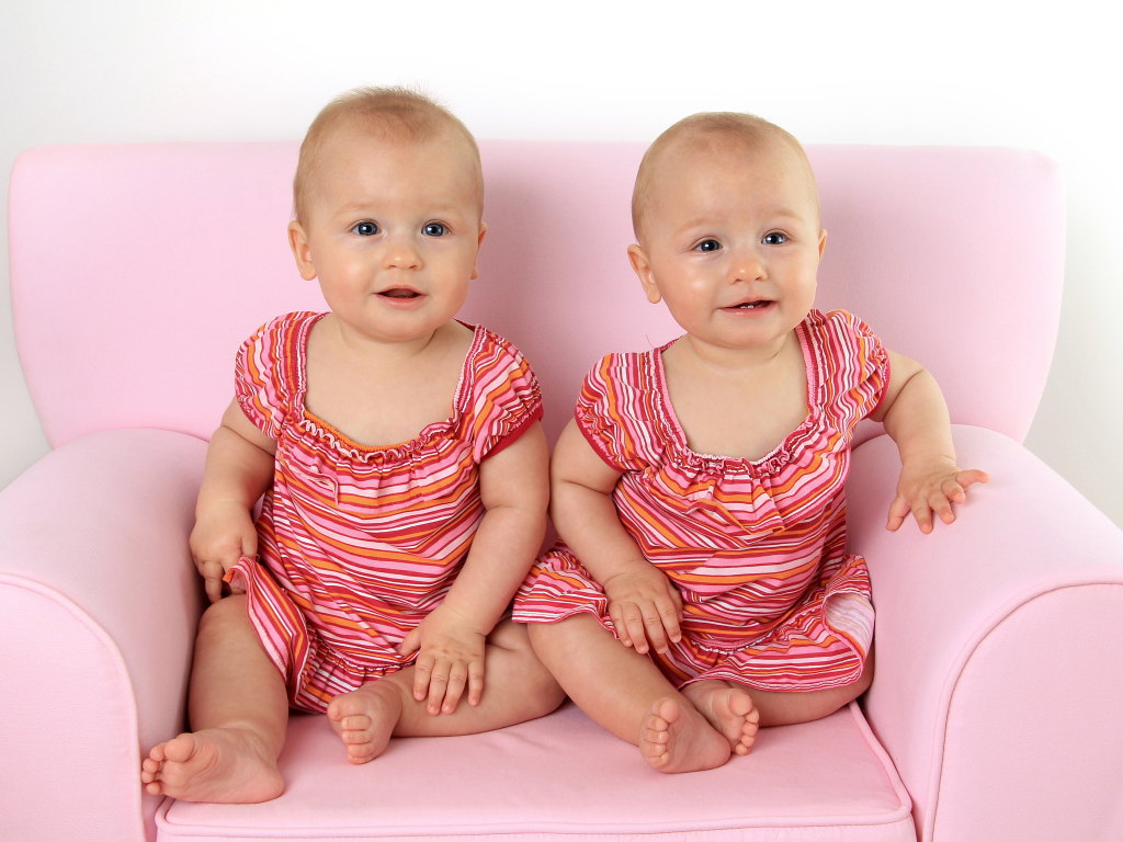 Две милые маленькие девочки сидят на розовом диване