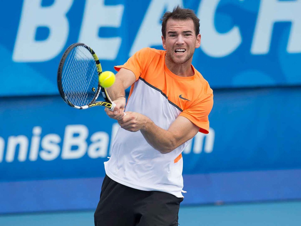 Теннисист Адриан Маннарино отбивает мяч ракеткой 