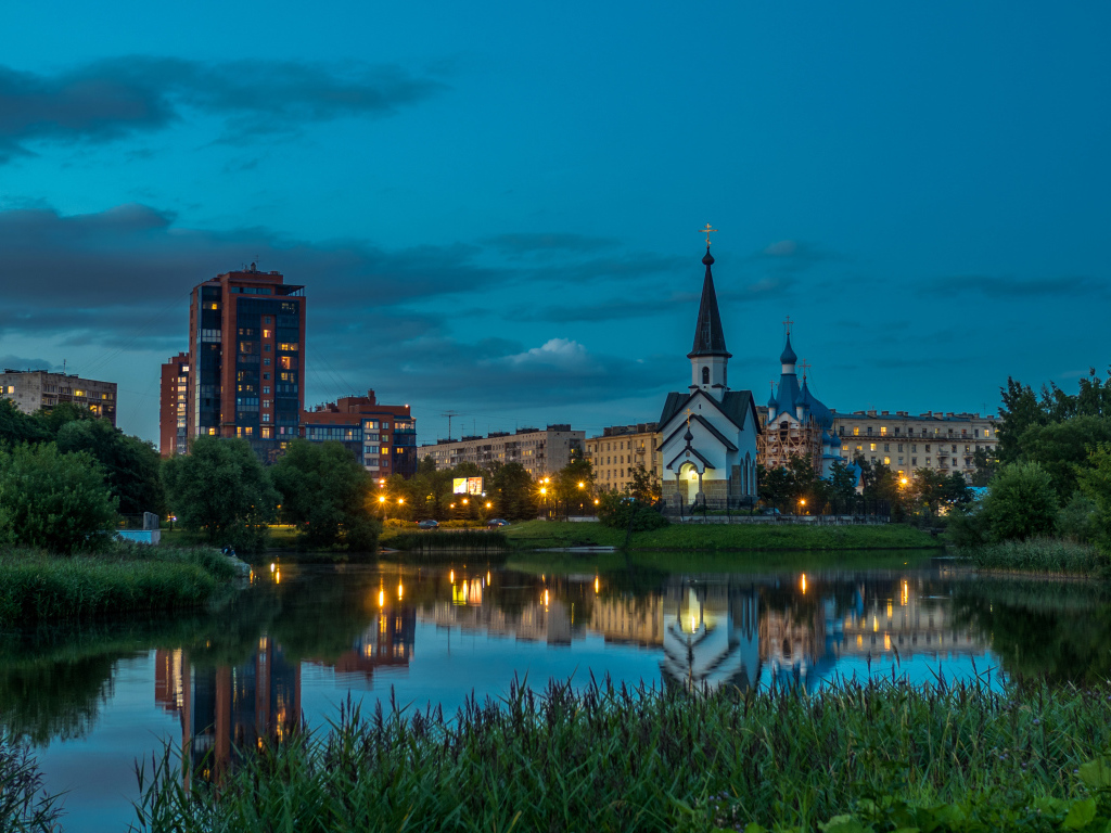 Вечерние огни маленькой церкви и домов отражаются в воде городского пруда, Санкт-Петербург. Россия