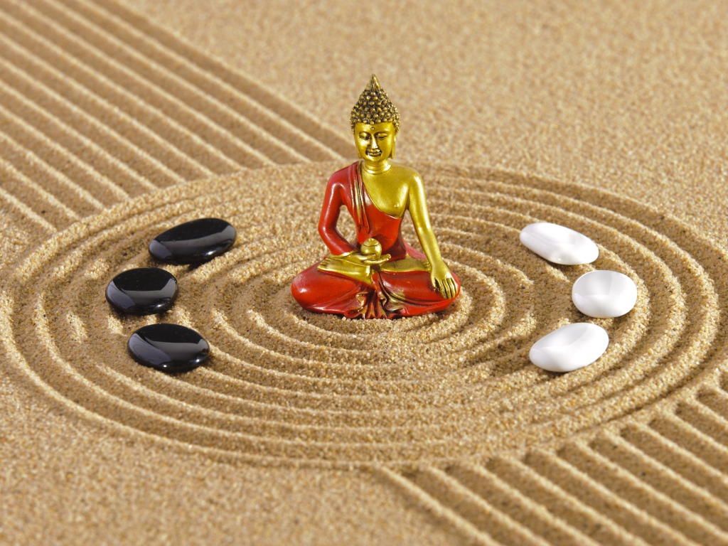 Статуэтка Будды стоит на песке с рисунком и камнями
