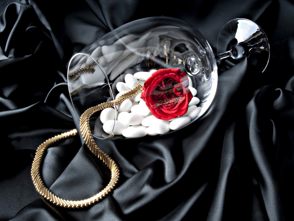 Бокал с золотой цепочкой, красной розой и белыми камнями на черном покрывале