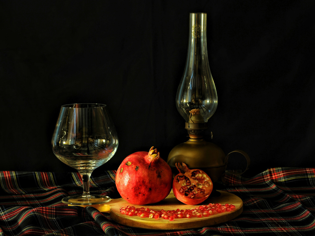 Керосиновая лампа, гранат и бокал на черном фоне
