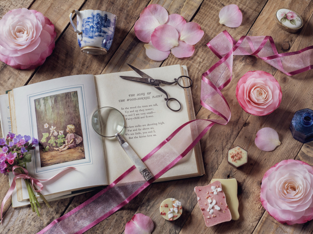 Старая книга на столе с увеличительным стеклом и искусственными цветами