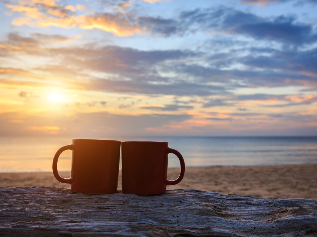 Две чашки стоят на песке на фоне рассвета 