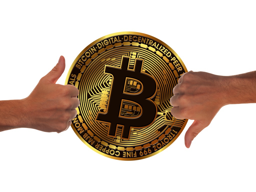 Two hands are evaluating a bitcoin coin on a white background.