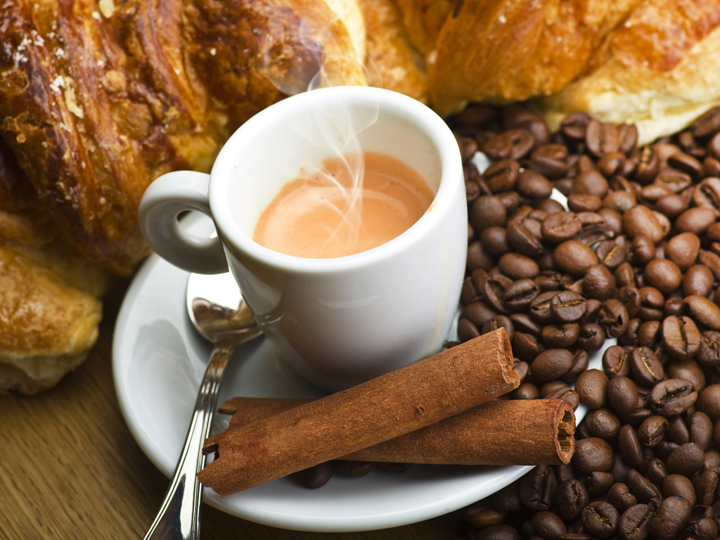 Чашка с горячим кофе на столе с корицей, зернами кофе и выпечкой