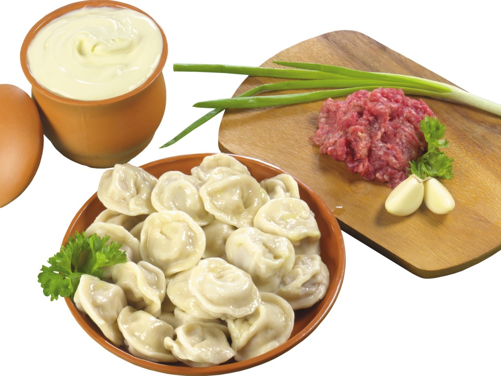 Вареные пельмени на столе с фаршем, сметаной и зеленым луком