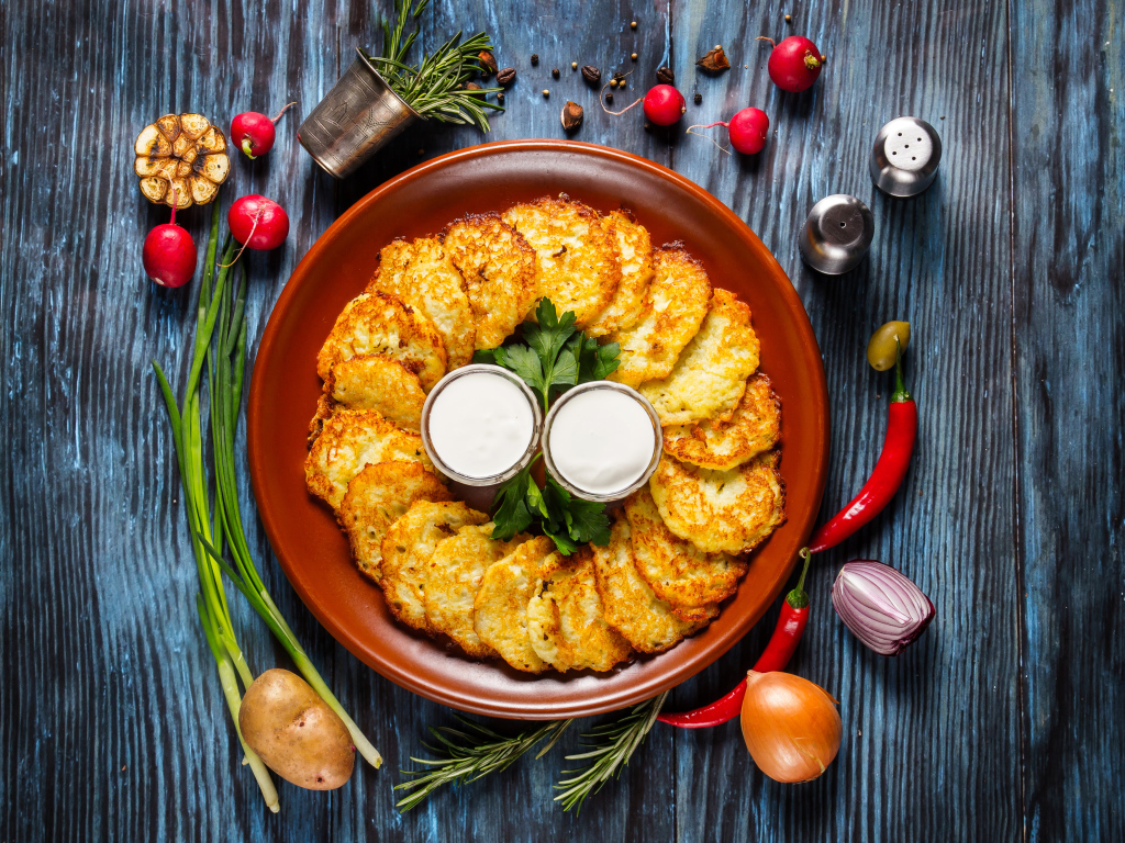 Драники с соусом на тарелке на столе с овощами