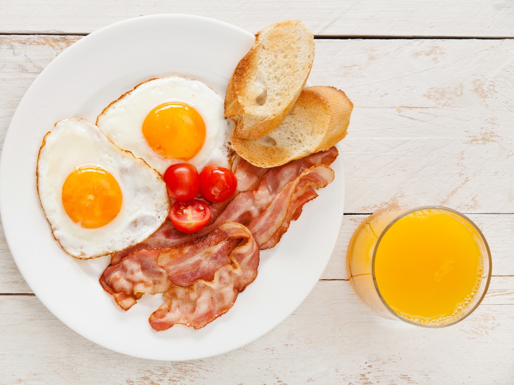 Яичница с беконом, гренками и помидорами на столе с соком 