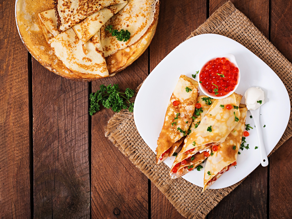 Рулетики из блинов на белой тарелке с красной икрой 