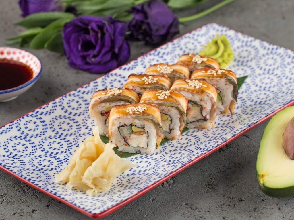 Роллы с авокадо и соевым соусом на столе с цветами 